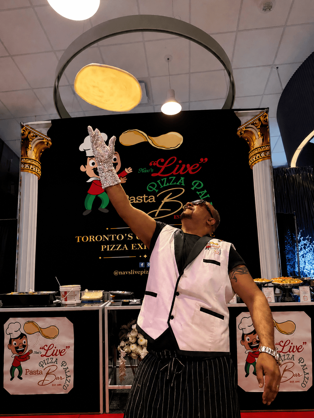 Nav's master chef tossing fresh pizza dough in the air in front of the branded Live Pizza Palazzo booth backdrop